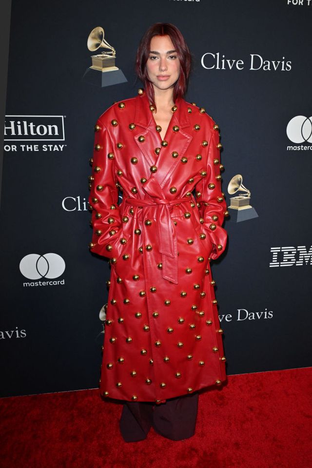 Dua Lipa at the Pre-Grammy Gala in a red Valentino leather trench coat adorned with gold baubles.